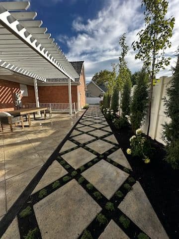 Elegant patio pathway with geometric stone design, lined by greenery and a pergola.