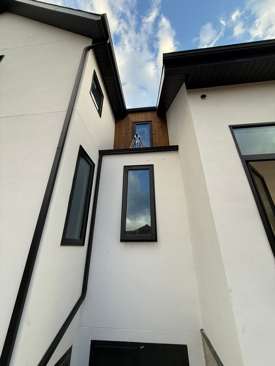 Modern house exterior with clean lines, large windows, and a wooden accent on the upper level.