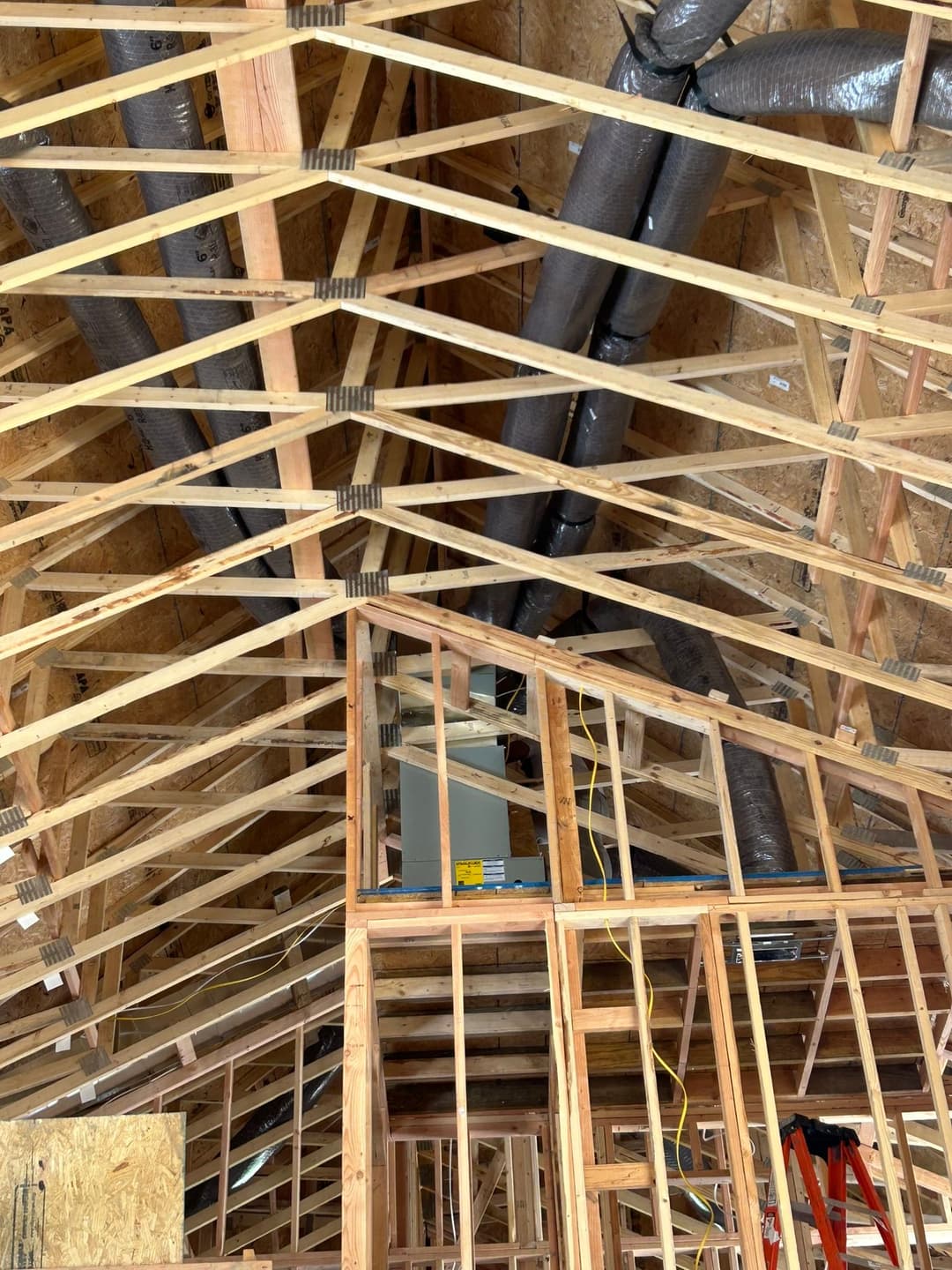 Interior view of a house under construction, showcasing wooden trusses and ductwork.