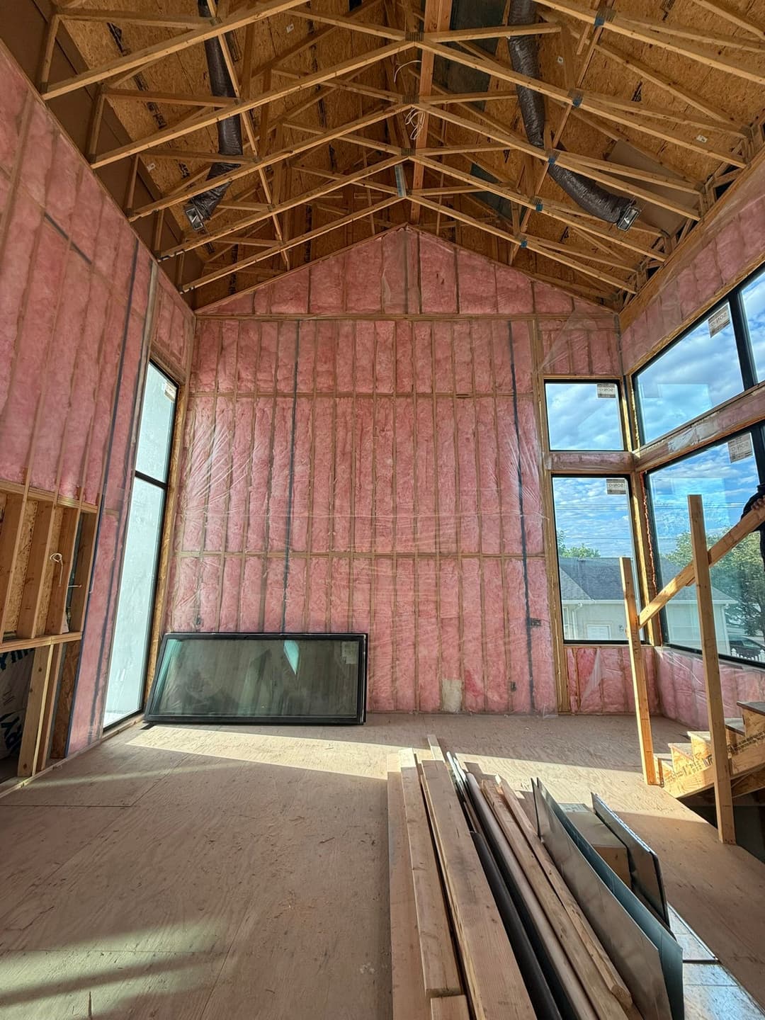 Interior of a partially finished home with pink insulation and large windows.