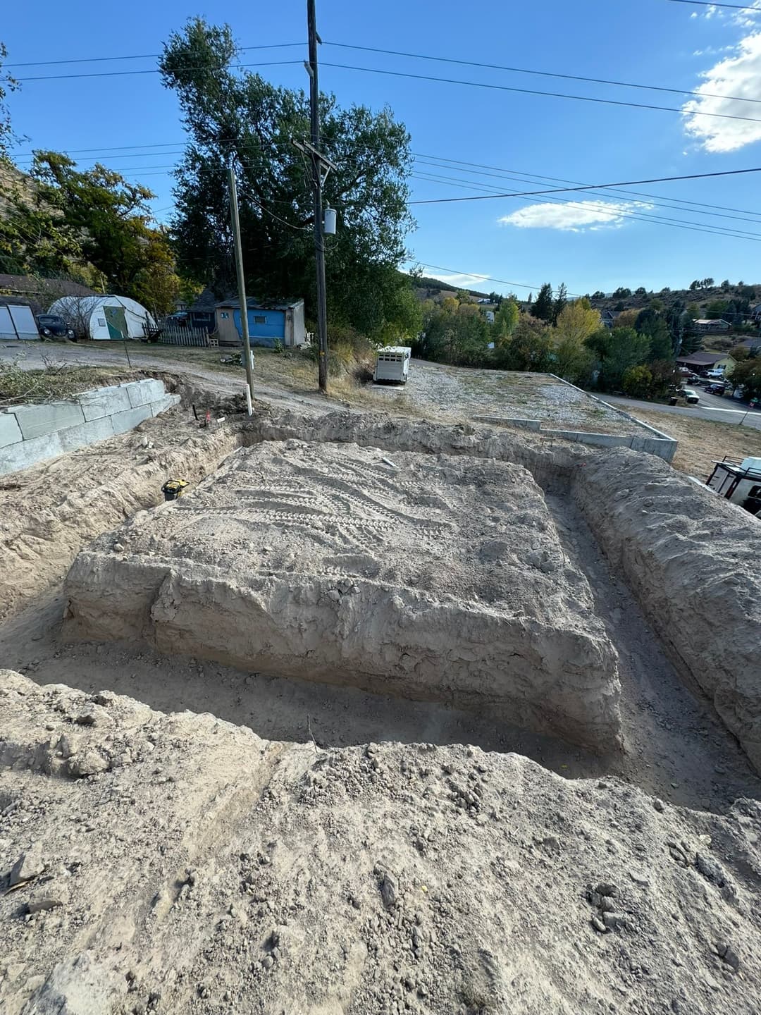Excavated foundation site with clear dirt outline and utility poles against a sunny sky.