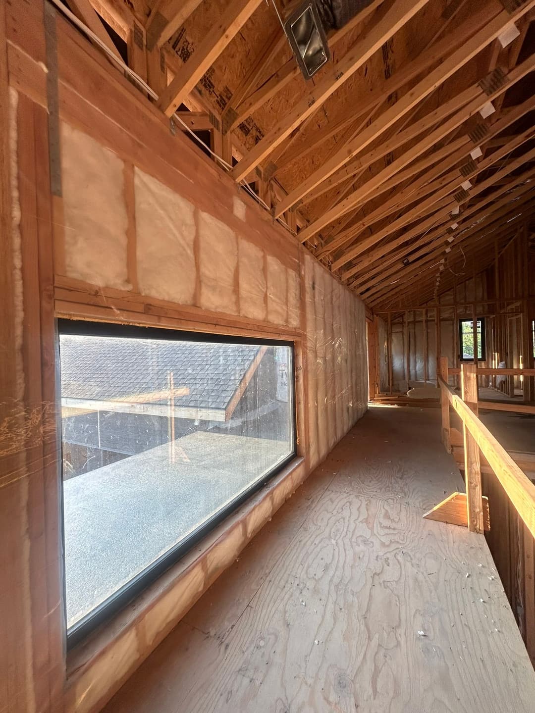 Interior view of a framed construction space with large window and exposed wooden beams.
