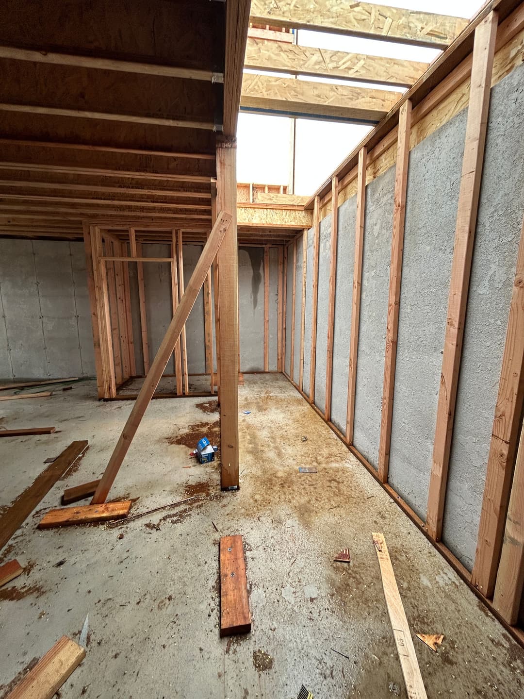Interior view of an unfinished building with wooden framing and concrete walls.
